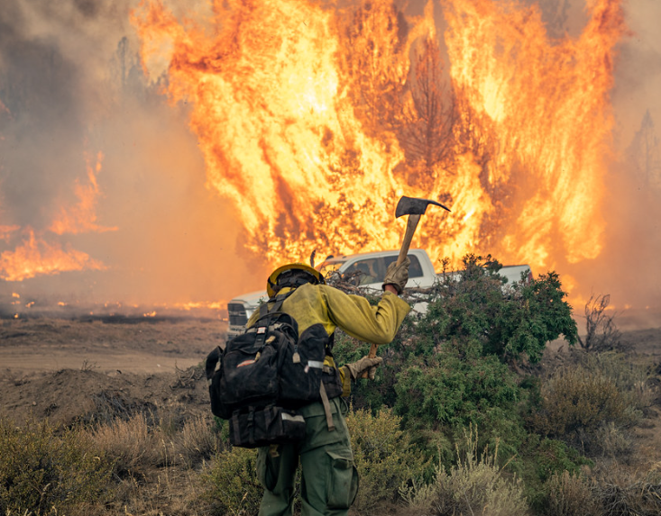 A firefighter swinging an ax with a fire in front of him