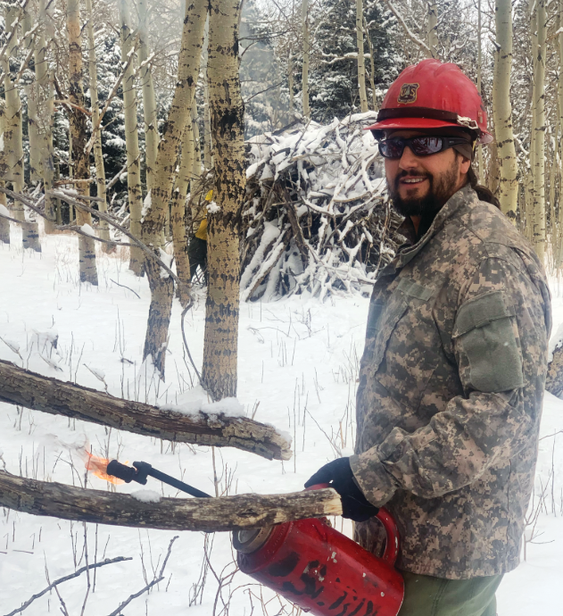 Alfonso Montoya holds a drip torch in a snowy forest.