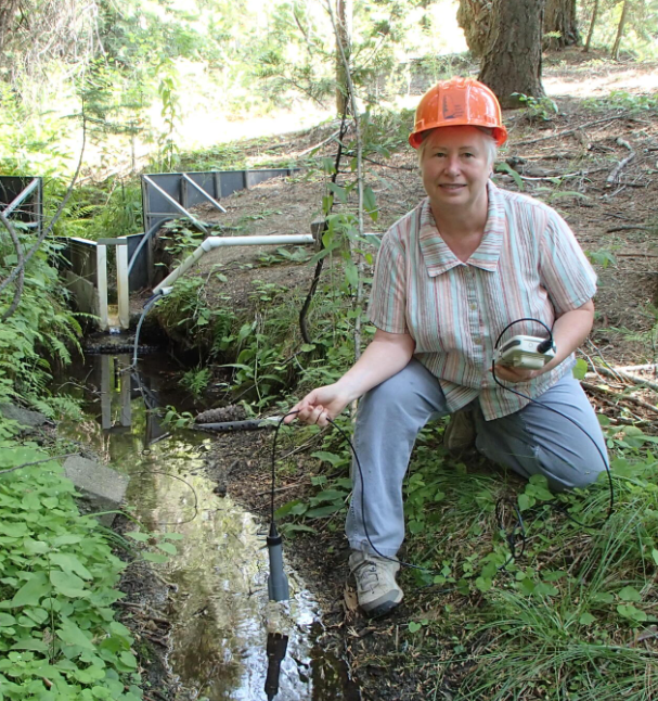 Carolyn Hunsaker kneels next to a stream.