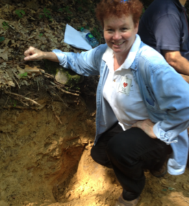 Mary Beth Adams kneels next to a bank of soil.