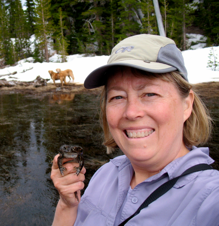 Dede Olson holds a frog by a body of water