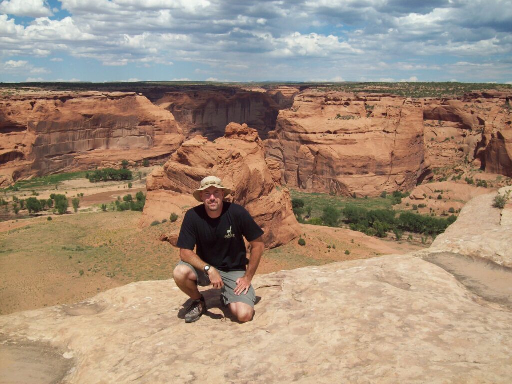 Scott Horn kneeling. There is a canyon behind him.