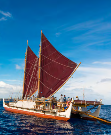 A large boat with several people aboard and two sails.
