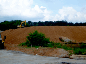 A mountain of fill dirt with an excavator on top of it.