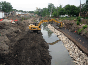 An excavator along a waterway placing rocks along a streambank