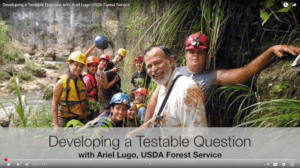 Thumbnail from the Developing a Testable QUestion YouTube video with Ariel Lugo. Features Ariels in a forest with other people wearing hardhats.