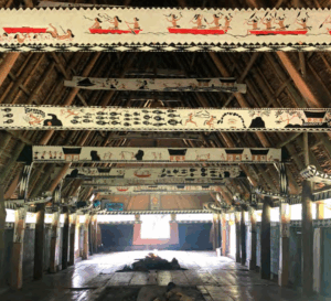 The interior of a Palauan long house called a bai. The beams overhead are decoratively painted, and there's a central fire pit.
