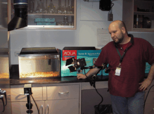 A scientist standing in front of an aquarium that has lights and cameras pointed at it