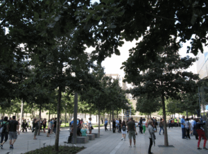 A memorial garden in New York City. There are people walking through the paved areas under many trees.