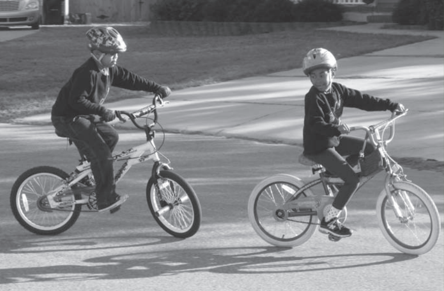 Two kids biking in the street wearing helmets
