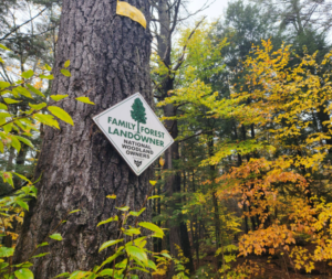 A sign on a tree in a forest reads "Family Forest Landowner, National Woodland Owners"
