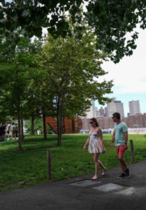 Two people walk on a path in the park by the Brooklyn Bridge