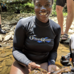 Dr. Barnett kneels in a stream bed and holds a hellbender
