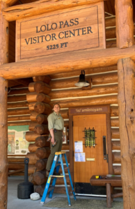 Sam Berglund standing on a latter under a Lolos Pass Visitor Center sign