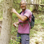 Dr. Schwartz stands in a pink t-shirt and back pack and pretends to claw a tree that shows scratch marks on its trunk.