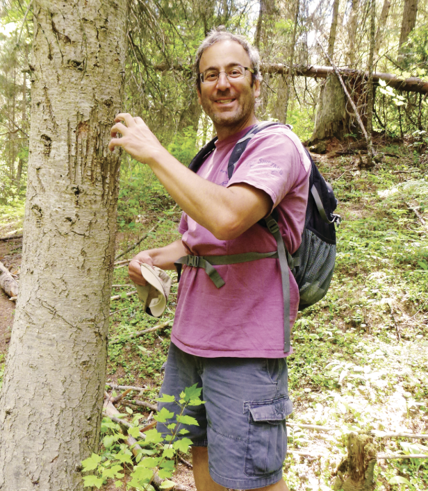 Dr. Schwartz stands in a pink t-shirt and back pack and pretends to claw a tree that shows scratch marks on its trunk.