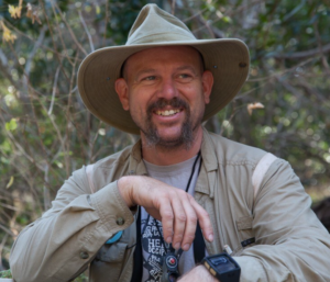 Dr. Booher sits outdoors in a wide-brimmed hat