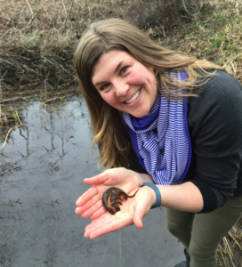 Dr. Penaluna holds salamanders and stands by a body of water.