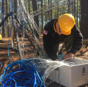 Dr. Clark kneels beside some equipment in a forest