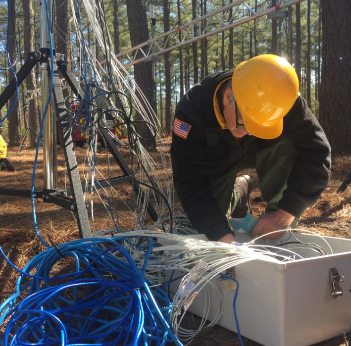 Dr. Clark kneels beside some equipment in a forest