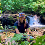 Alexa Scanlan in a forested area with a waterfall behind her