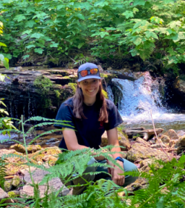 Alexa Scanlan in a forested area with a waterfall behind her