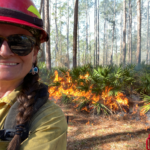 Angie Matos in fire gear in front of a prescribed burn in the forest