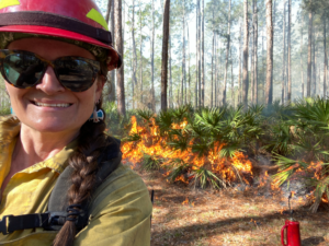 Angie Matos in fire gear in front of a prescribed burn in the forest