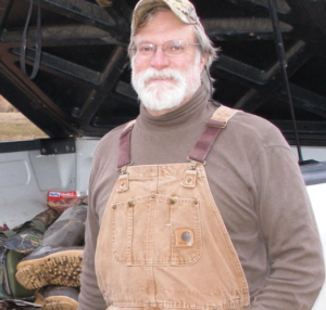 Dr. Warren wears overalls and stands in front of a pickup truck bed.