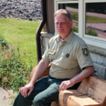 Mr. Hughes sits on a bench outside a visitor center.