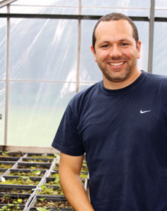 Dr. Royo stands beside seedlings in a greenhouse.