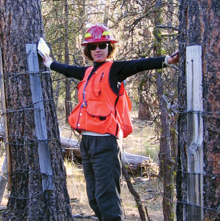 Dr. Kerns stands with her arms outstretched between two trees.