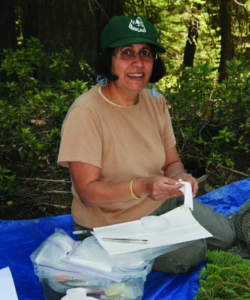 Dr. Minocha sits on a blue tarp in a forest and processes samples.