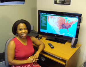 Erika Cohen at a desk with a map on a screen behind her