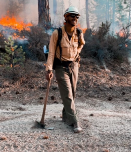 Jordan Gulley in fire protective gear holding an ax outside