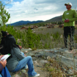Dr. Iniguez stands on a mountainside and talks to a group of students