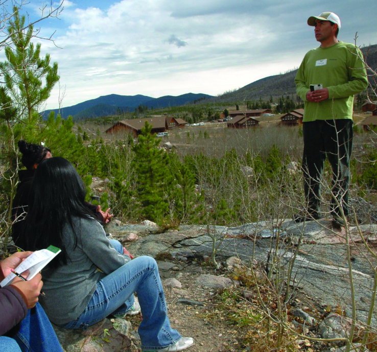 Dr. Iniguez stands on a mountainside and talks to a group of students