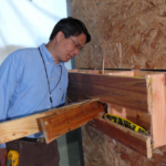 Dr. Cai holds a cordless drill and examines a structure built of lumber