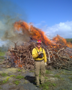 Matt Jolly in protective gear standing in front of a burnpile