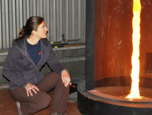 Dr. McAllister kneels next to a tall cylinder containing a column of fire.