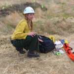 Olivia Collette Outside with a hard hat and a bag fool of instruments and tools