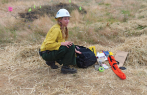 Olivia Collette Outside with a hard hat and a bag fool of instruments and tools