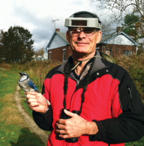 Dr. Arendt holds a blue jay and wears binoculars
