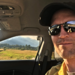 Portrait of Paul Corrigan in a car with mountains outside the window