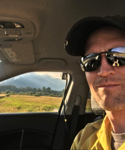 Portrait of Paul Corrigan in a car with mountains outside the window