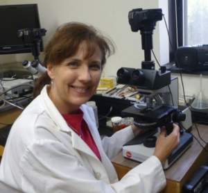 Ms. Cram sits at a microscope in a lab coat
