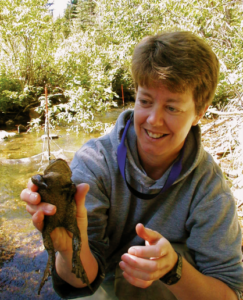 Susie Adams outside by a body of water holding up a frog