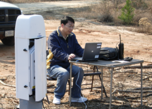 Liu sitting at a desk outside with meteorology equipment and a computer