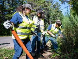 Kids and adults wear safety vests and work beside a road.