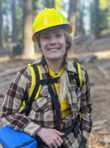 Emily Brodie wears a yellow safety helmet and a backpack in the forest.